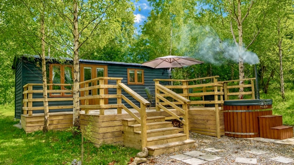 Luxury shepherd’s hut with a raised decked area, seating and a hot tub to the front of the hut, located at MArtin’s Meadow in Crossgar, County Down.